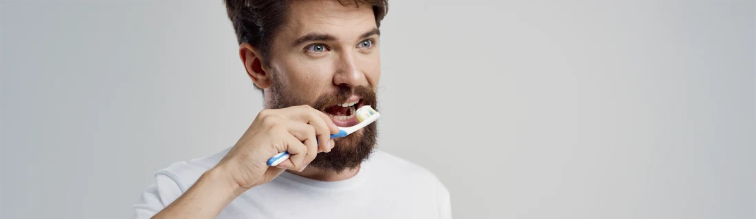 Person brushing teeth with a blue toothbrush, wearing a white shirt, against a light gray background.